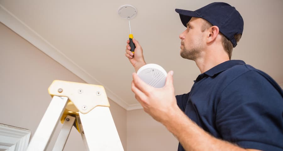 Man placing fire alarm on ceiling of home